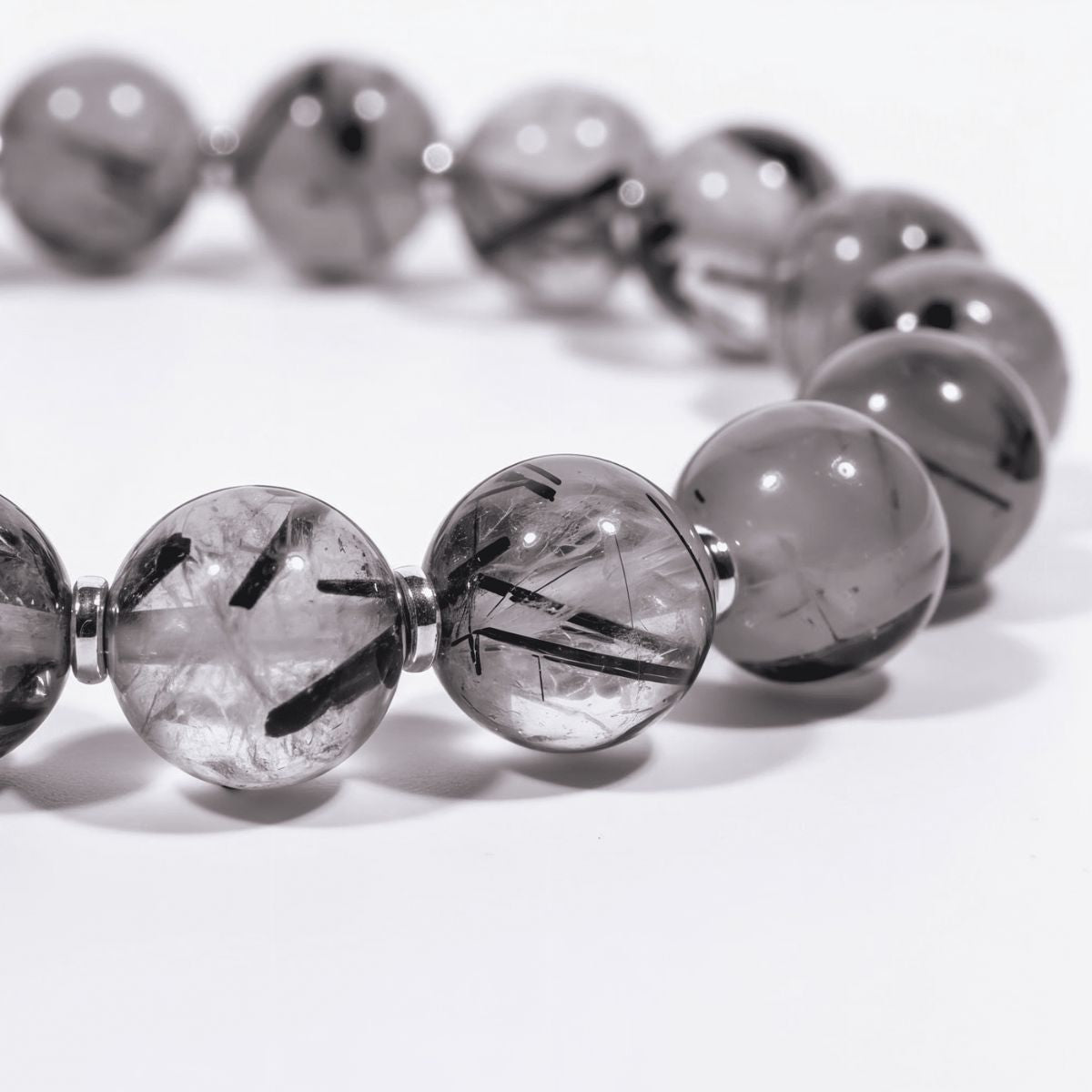 Close-up detail of natural black rutilated quartz beads with striking black needle inclusions, glossy depth, and polished metal spacers.