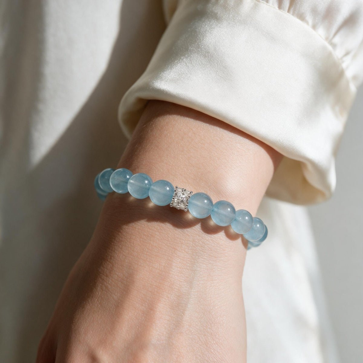 Woman styling the soft blue Coastal Elegance aquamarine bracelet with a neutral white outfit.