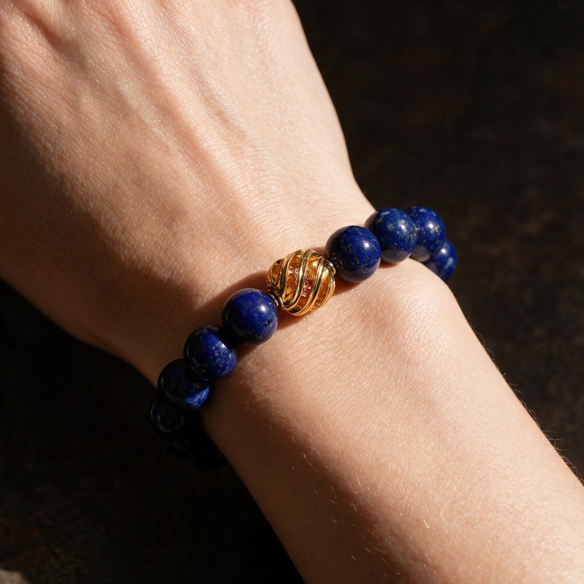 Natural lapis lazuli bracelet worn on the wrist in warm shadow with its gold-plated centerpiece visible.