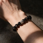 Midnight Shield black obsidian bracelet worn on a woman’s wrist in warm shadowed light.