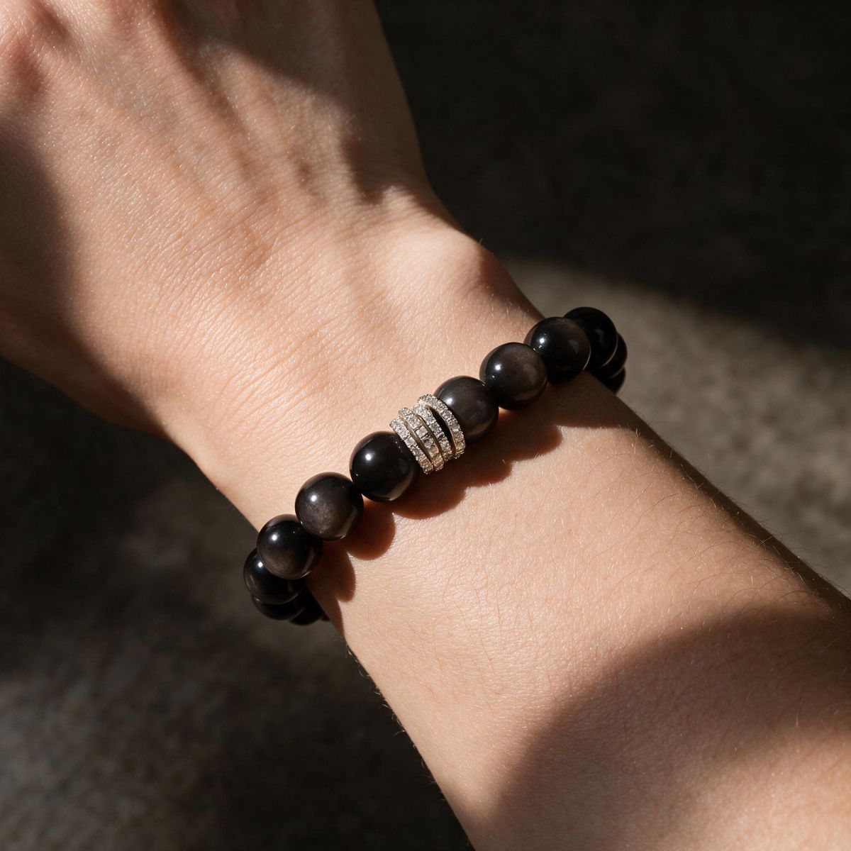 Midnight Shield black obsidian bracelet worn on a woman’s wrist in warm shadowed light.