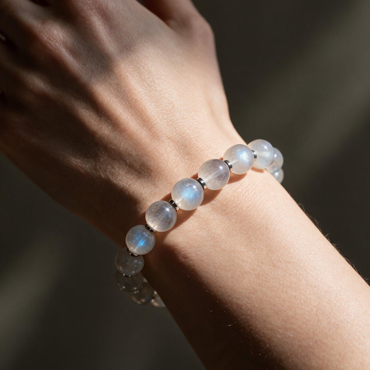 Natural moonstone bracelet worn on a woman’s wrist with subtle blue flashes visible in warm light