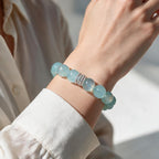 Ocean Calm natural Brazilian aquamarine bracelet with 12mm ocean-blue beads and a silver-tone centerpiece worn with a white blouse.