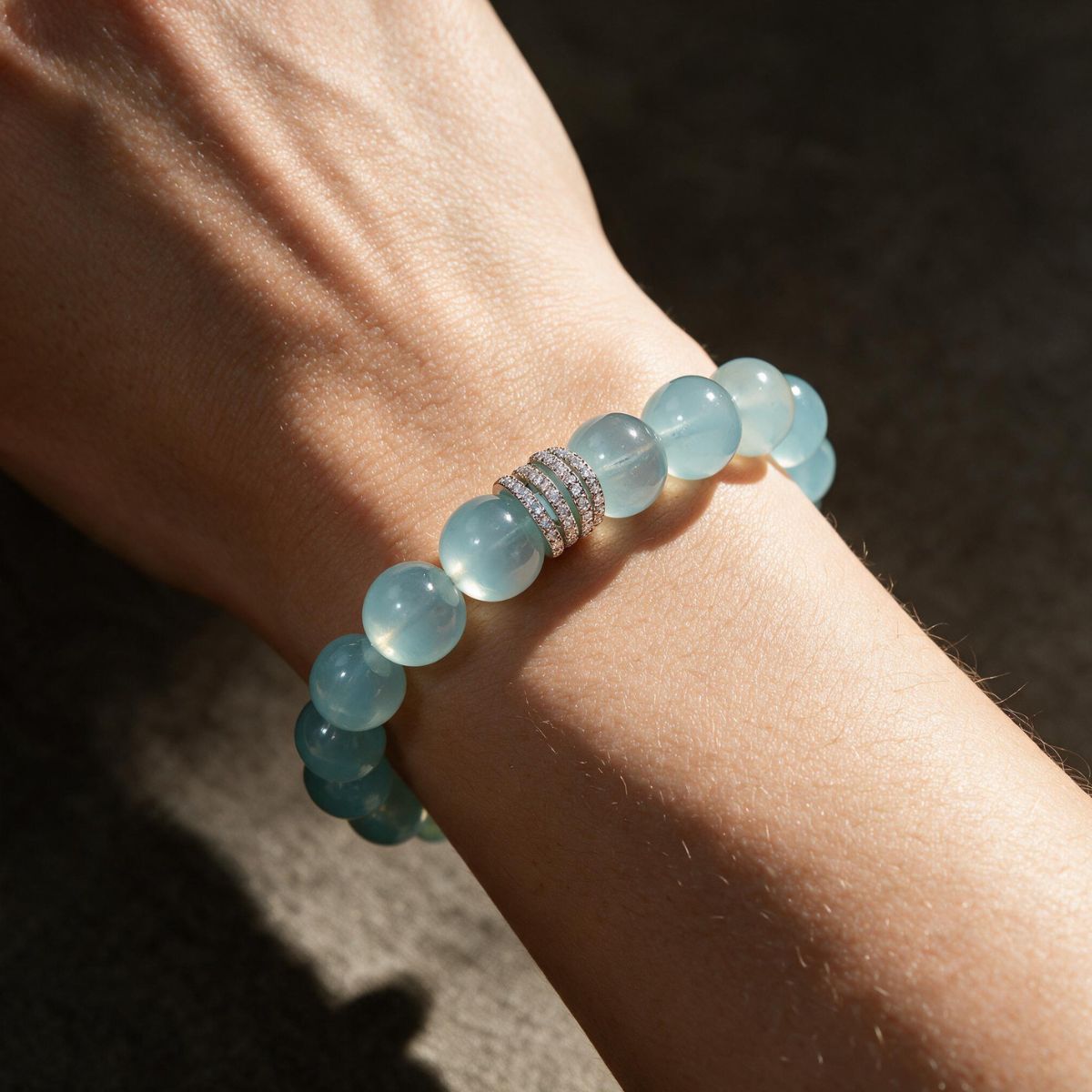 Ocean Calm natural Brazilian aquamarine bracelet with 12mm ocean-blue beads and a silver-tone centerpiece worn on a woman’s wrist in sunlight.