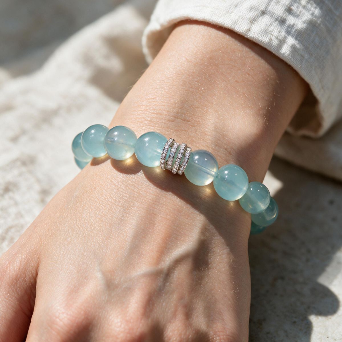 Ocean Calm natural Brazilian aquamarine bracelet with 12mm ocean-blue beads and silver-tone detail worn on a woman’s wrist in sunlight.