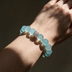 Close-up of the Ocean Calm natural Brazilian aquamarine bracelet on a woman’s wrist in sunlight, showing 12mm blue beads and silver-tone detail.
