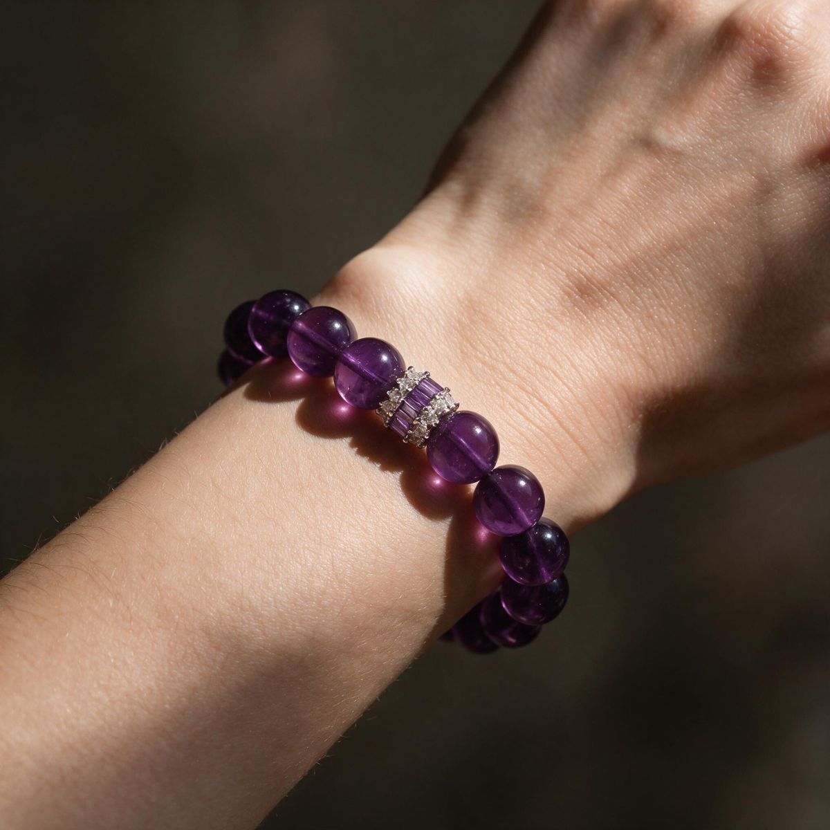 Deep violet amethyst bracelet styled on a woman’s wrist against a dark background.
